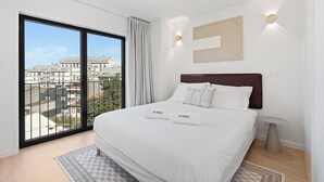 Un dormitorio moderno con una cama grande, vistas de edificios a través de un ventanal de pared a techo, y una decoración minimalista.