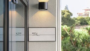 Fachada de edificio con un muro texturizado, un accesorio de luz negro fijado a la pared y un letrero con la inscripción 'KEEP calm'.