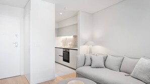 Una sala de estar moderna con un sofá gris, una mesa redonda y una cocina al fondo.