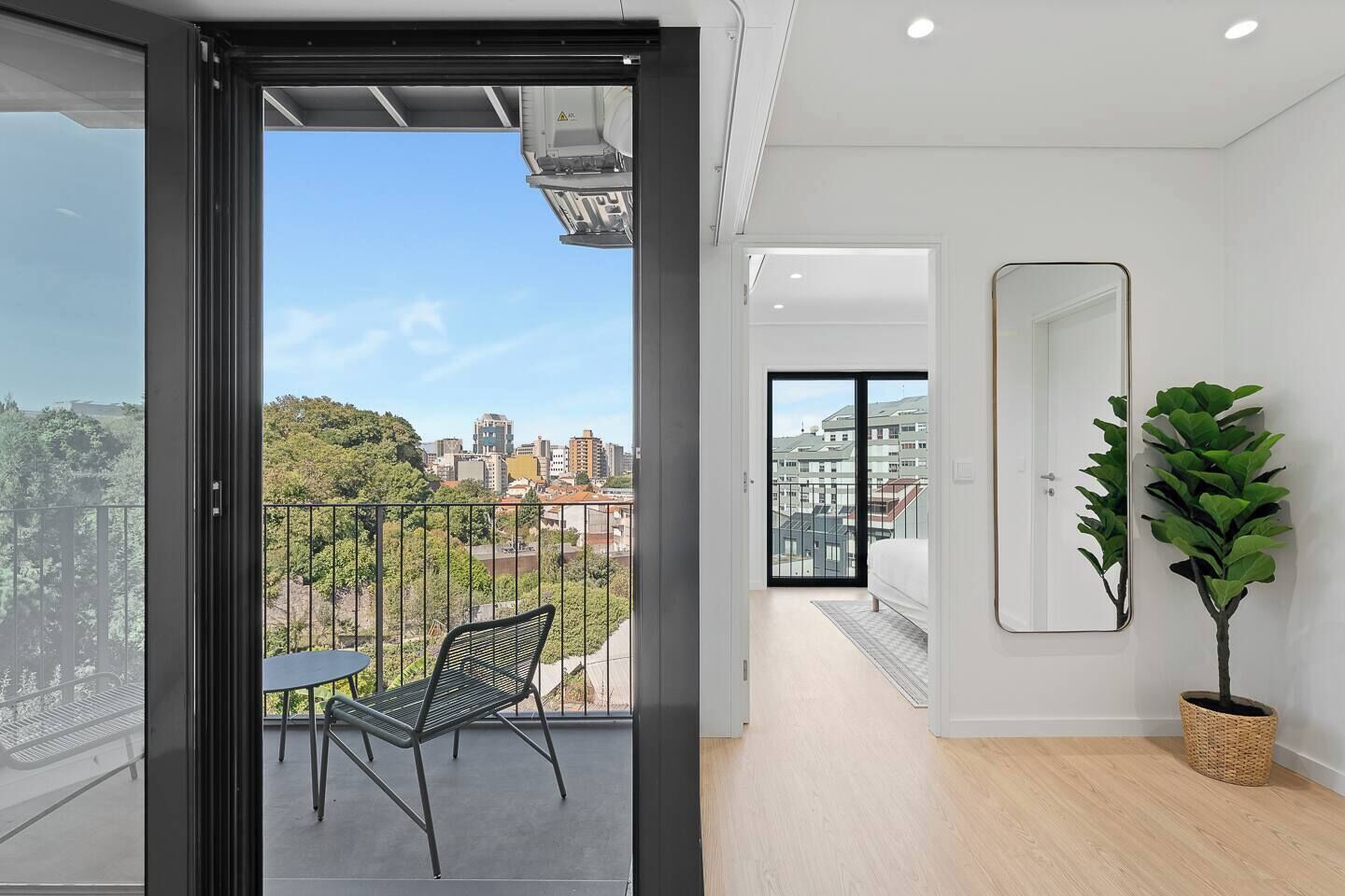 Eine moderne Wohnung mit Balkon, einem Esstisch, einem Stuhl, einem Blumentopf und Blick auf die Stadt.