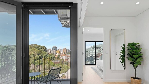 Un apartamento moderno con balcón, una mesa de comedor, una silla, una planta en maceta y vistas a la ciudad.