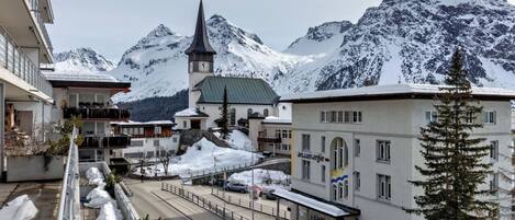 Un pueblo cubierto de nieve con una iglesia, una carretera y montañas al fondo.