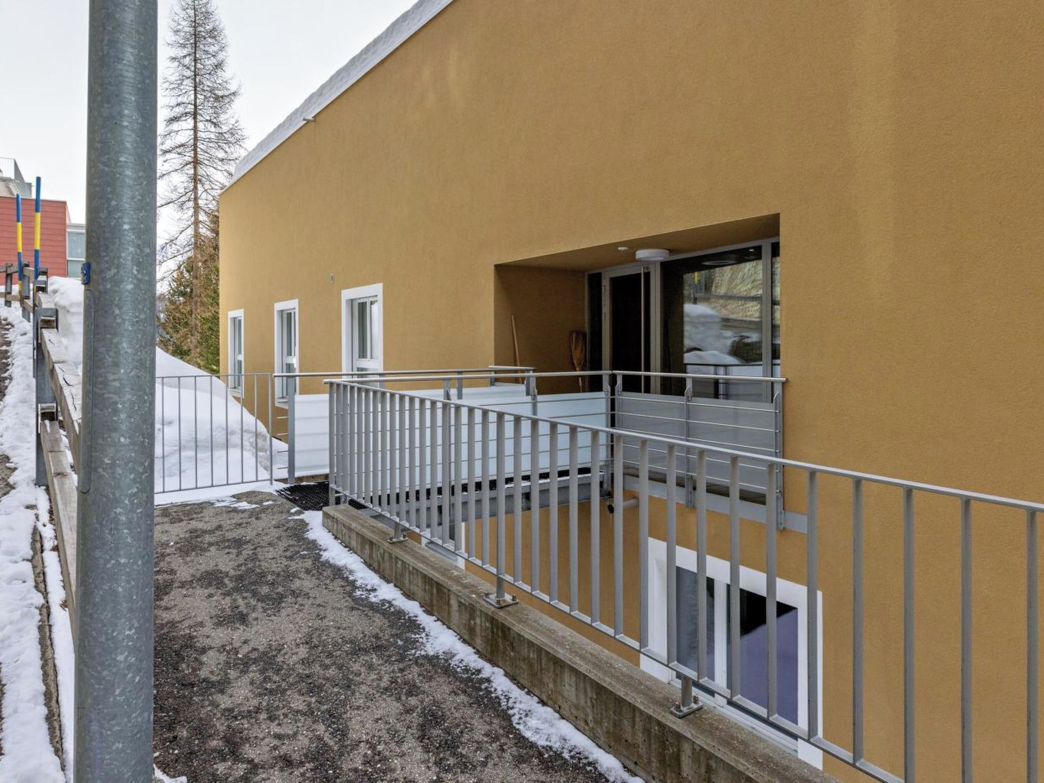 Ein Gebäude mit gelber Fassade, einem Metallgeländer und einem Fenster mit Blick auf eine verschneite Landschaft.