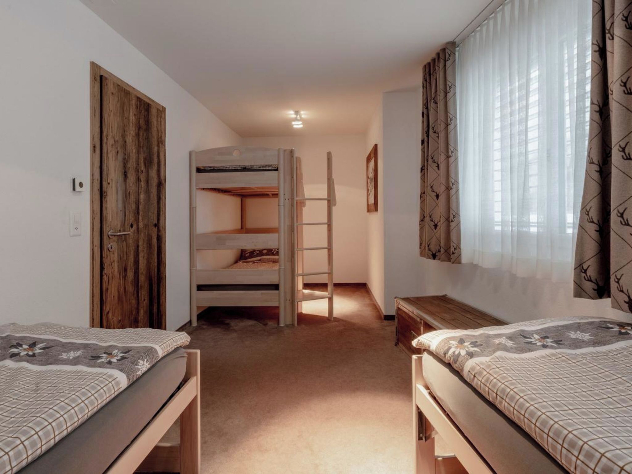 A room with two beds, a wooden wardrobe, a ladder, and a bunk bed in the background.