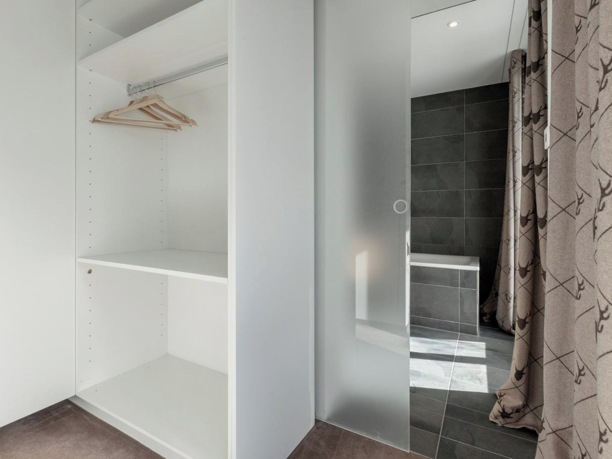 Une chambre d’hôtel dotée d’un dressing, d’un espace douche et d’une salle de bain aux carreaux foncés.