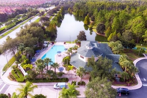Eine Vogelperspektive zeigt eine Wohngegend mit einem Schwimmbad, einem Haus mit außergewöhnlichem Dach und einem von Bäumen umgebenen See.