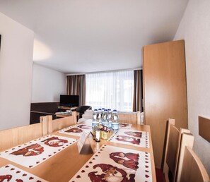 A hotel room with a dining table set for two, a TV, and a window with curtains. - Haus Camillo Appartement/Fewo 6-Bettwohnung Nr. 14 by Interhome (Saas-Fee)