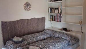 Quarto com uma cama, uma estante de livros e piso de madeira.