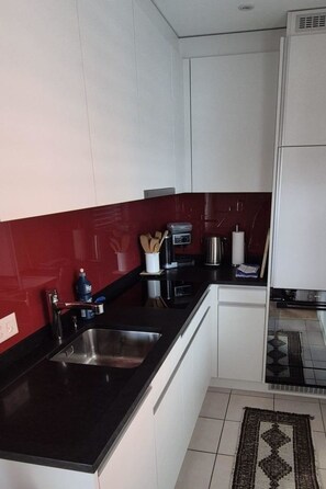A kitchen with a black countertop, white cabinets, a red backsplash, and a stainless steel sink. - Casa Cresta B72 Appartement/Fewo,  , 2-Bettwohnung 2-Bettwohnung by Interhome (Arosa)