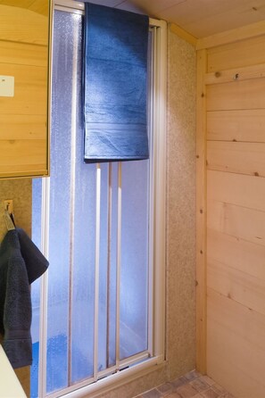 Une salle de bain avec une porte de douche en verre dépoli, un porte-serviettes avec une serviette, et des murs en bois.
