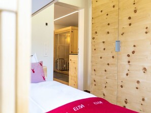 A hotel room with a bed, a wooden wardrobe, and a door leading to a bathroom. - Elsa Appartement/Fewo, Dusche oder Bad, WC, 2 Schlafräume by Interhome (Arosa)