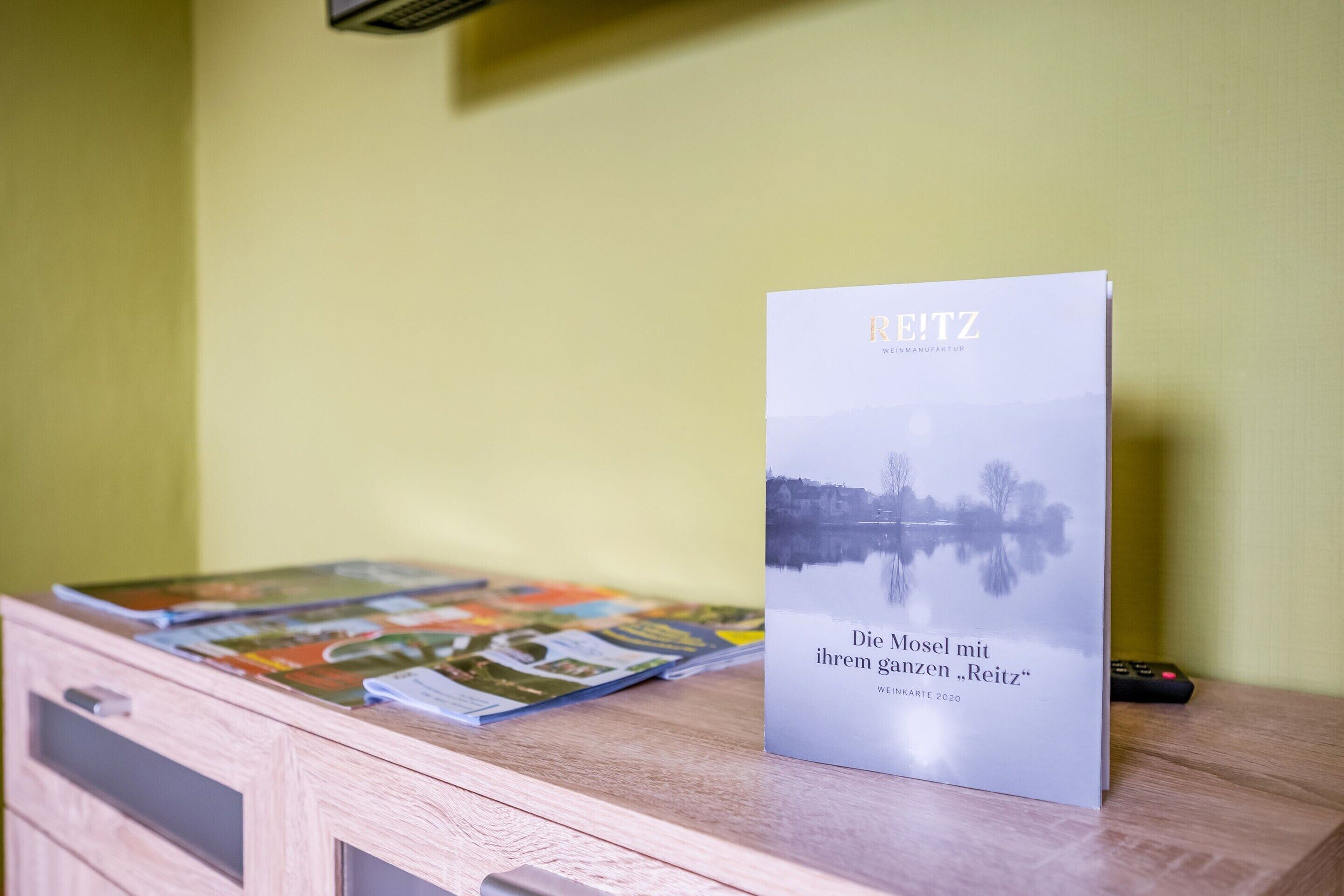 A book titled 'Die Mosel mit ihrem grenzen 'Reitz'' on a wooden table with magazines.