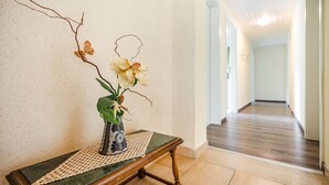 Ein Flur mit einer Holzbank, einer Blumenvase und einer strukturierten Wand.