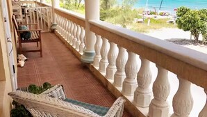 Een balkon met rieten meubels, een witte balustrade en uitzicht op het strand.
