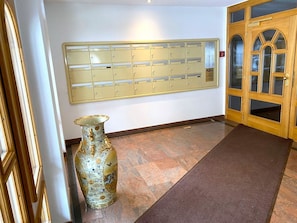 Ein Flur mit einem großen Wandbriefkasten, einer dekorativen Vase und einer Holztür mit Glasfeldern.