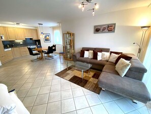 Ein modernes Wohnzimmer mit einem grauen Sofa, einem Glastisch und einem Essbereich mit Holztisch und Stühlen.