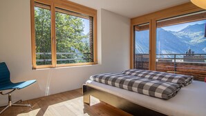 A bedroom with a bed, a chair, and large windows with mountain views. - Salis 06 by Arosa Holiday Appartement/Fewo, Dusche und Bad, WC, 3 Schlafräume by Interhome (Arosa)