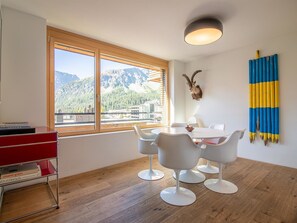 A modern room with a wooden floor, a dining table with white chairs, a red desk, and a large window with a mountain view. - Salis 06 by Arosa Holiday Appartement/Fewo, Dusche und Bad, WC, 3 Schlafräume by Interhome (Arosa)