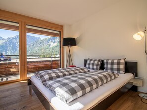 Ein Schlafzimmer mit einem großen Bett, einem Nachttisch, einer Lampe und Blick auf Berge durch eine Schiebetür.