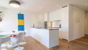 A modern kitchen with white cabinetry, a central island, and a dining area with white chairs. - Salis 06 by Arosa Holiday Appartement/Fewo, Dusche und Bad, WC, 3 Schlafräume by Interhome (Arosa)