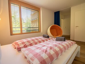 A bedroom with two beds, a large window with blinds, a hanging chair, and a door leading to another room. - Salis 06 by Arosa Holiday Appartement/Fewo, Dusche und Bad, WC, 3 Schlafräume by Interhome (Arosa)