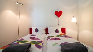 A double bed with a colorful bedspread, two pillows, a red heart decoration on the wall, and bedside lamps. - Salis 06 by Arosa Holiday Appartement/Fewo, Dusche und Bad, WC, 3 Schlafräume by Interhome (Arosa)