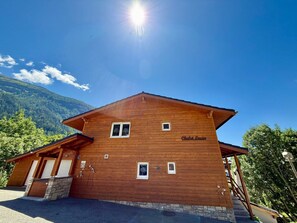 A wooden chalet with a sign reading 'Chalet Lucia,' a stone staircase, and a view of a forested mountain. - Chalet Lucia 1 (EG) # 3-bed apartment, Dusche, WC 3-bed apartment, Dusche, WC by Interhome (Leukerbad)