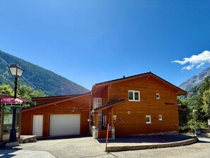Ein Holzhaus mit Garage und überdachter Veranda, vor einer Bergkulisse.