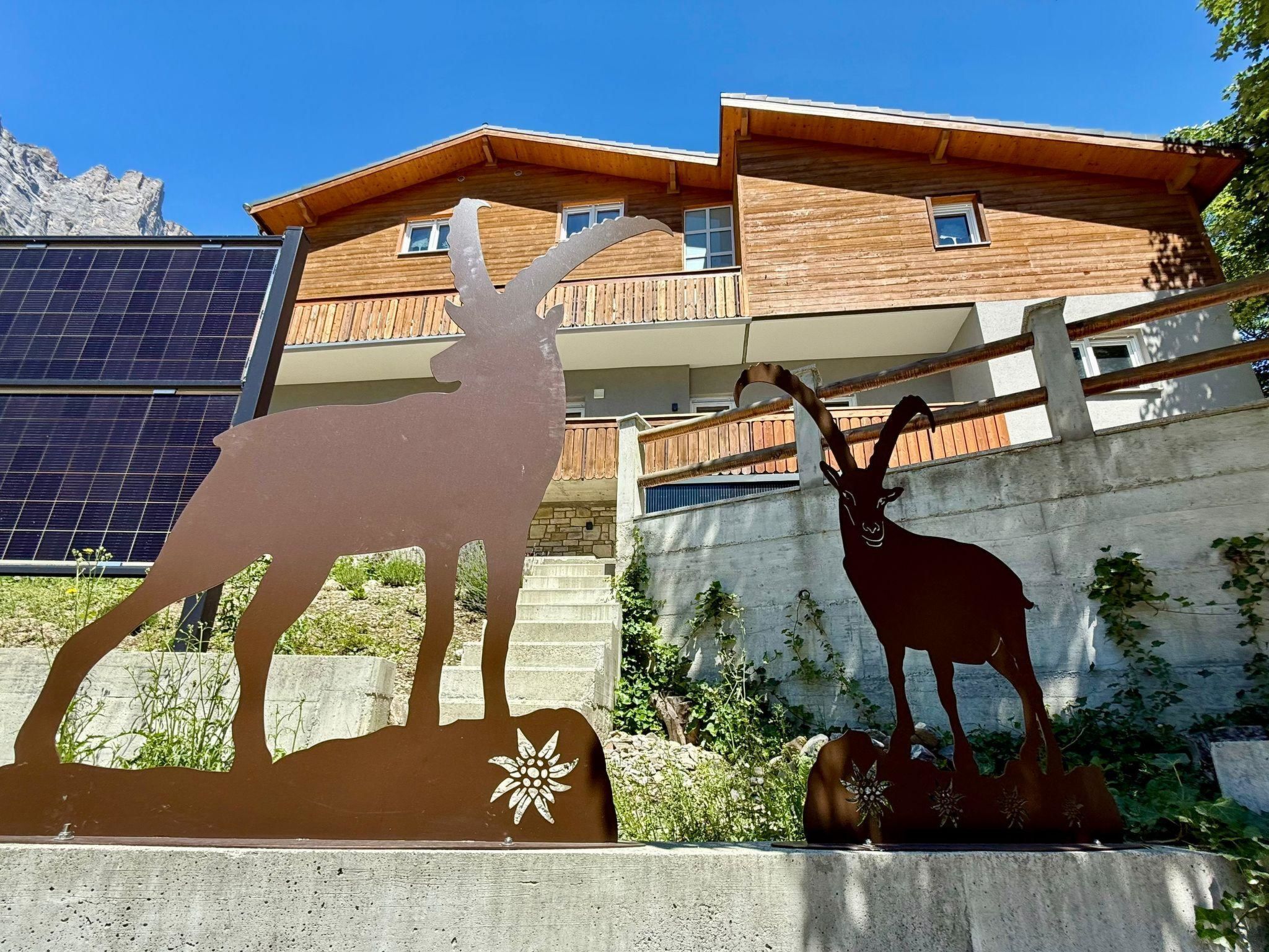 A building with a wooden facade and balconies, a metal sculpture of a deer, and solar panels in the background.