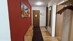 Een gang met een houten bankje, een rode muur en een deur met een spiegel.