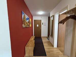A hallway with a wooden bench, a red wall, and a door with a mirror. - Apollo 50 # 4-bed apartment, Bad, WC 4-Bettwohnung, Bad, WC by Interhome (Leukerbad)