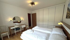 Een slaapkamer met een tweepersoonsbed, een bureau met stoel, een garderobe en een spiegel.