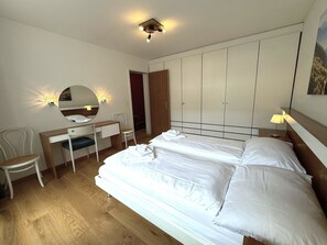 A bedroom with a double bed, a desk with a chair, a wardrobe, and a mirror. - Apollo 50 # 4-bed apartment, Bad, WC 4-Bettwohnung, Bad, WC by Interhome (Leukerbad)
