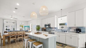 Eine moderne Küche mit weißen Schränken, einer zentralen Kochinsel mit Barhocker, Pendelleuchten und einem Essbereich mit Holztisch und Stühlen.