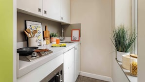 Cocina compacta con armarios blancos, estufa, pileta y una planta en maceta.