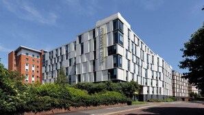 Un edificio moderno con un llamativo letrero que dice 'UNITED STUDENTS', con fachadas de ladrillo y vidrio, y rodeado de vegetación.