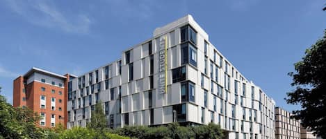 Edifici modern amb un distintiu rètol 'UNITED STUDENTS', façanes de maó i vidre, i envoltat de vegetació.