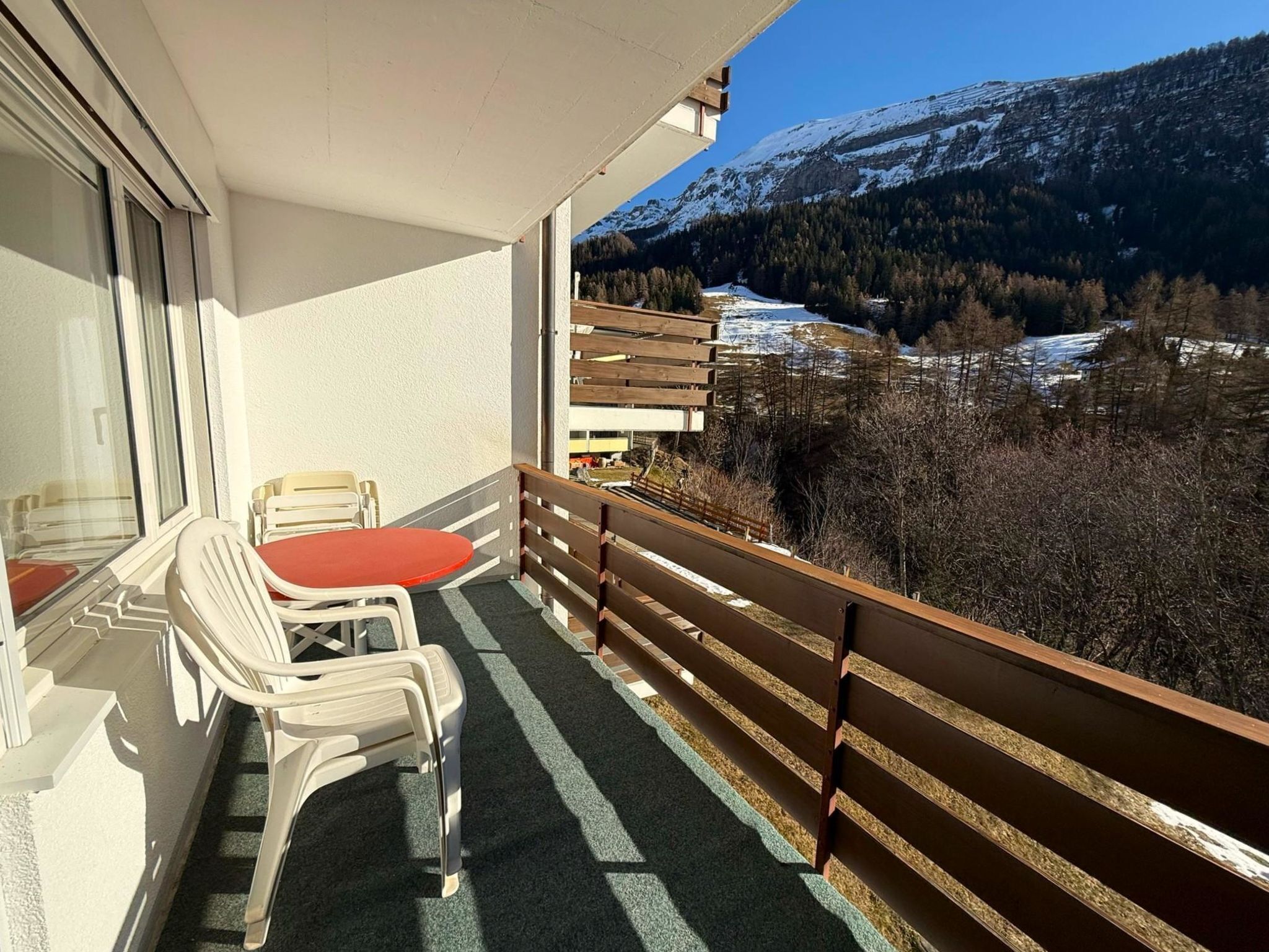 Ein Balkon mit Tisch und Stühlen mit Blick auf eine verschneite Berglandschaft.