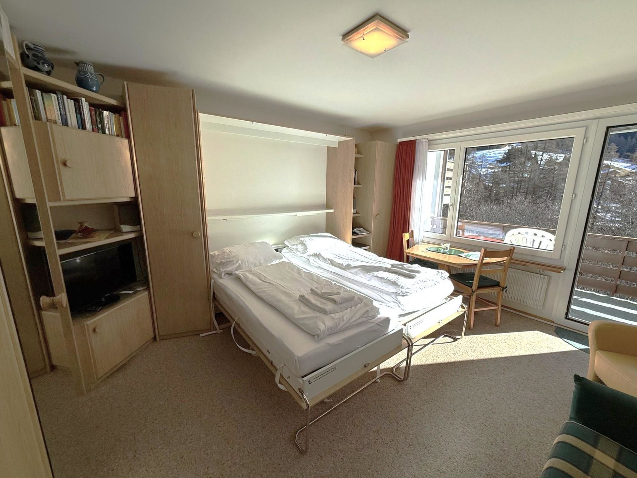 Une chambre d’hôtel de taille réduite, comprenant un lit simple, une table de chevet et un petit bureau avec une chaise.