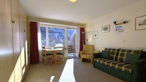 Et værelse med sofa, spisebord med stole, en radiator og et vindue med gardiner.