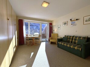 A room with a sofa, a dining table with chairs, a radiator, and a window with curtains. - Apollo 47 # 2-bed apartment, Dusche, WC 2-Bettwohnung, Dusche, WC by Interhome (Leukerbad)