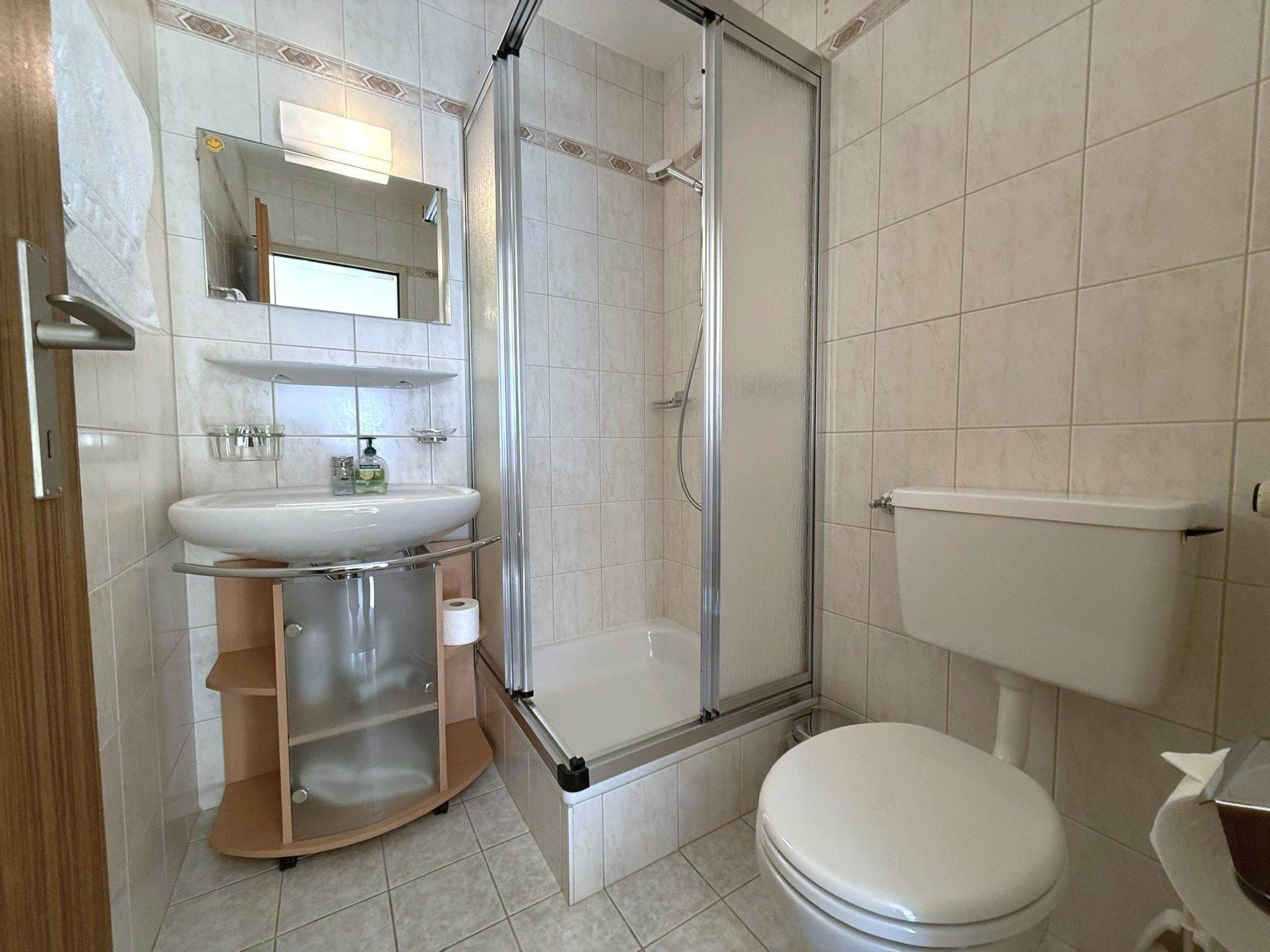 Et badeværelse med bruser, toilet, håndvask og spejl.