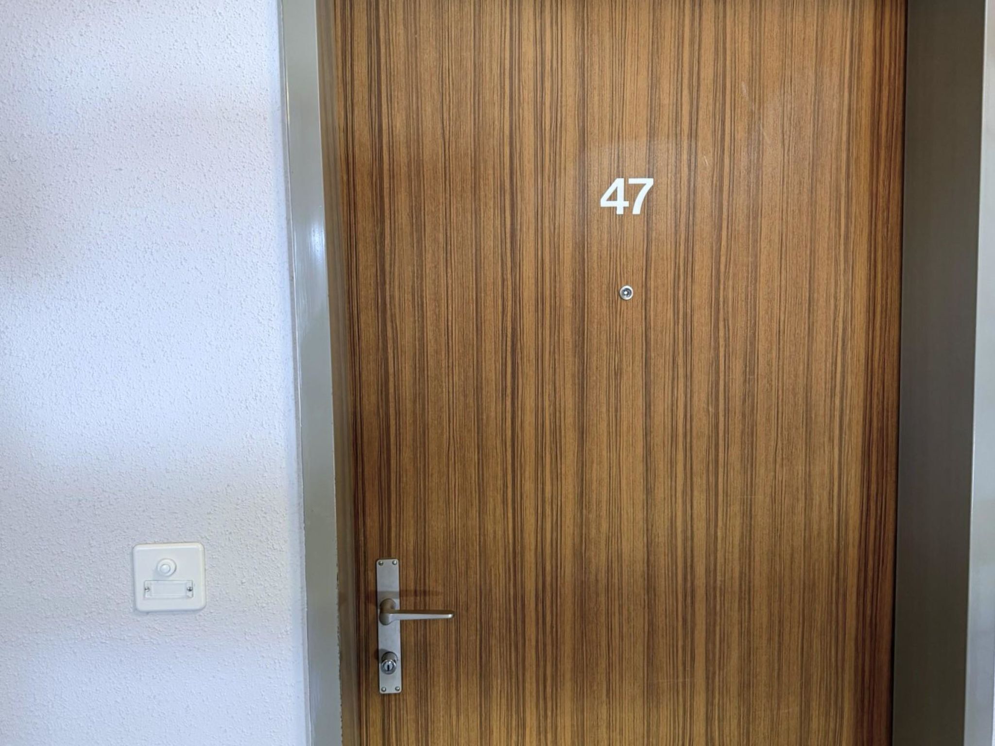Een houten deur met het nummer 47, een deurklink en een lichtschakelaar op de muur.