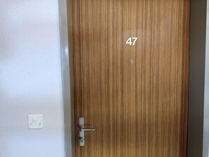 Een houten deur met het nummer 47, een deurklink en een lichtschakelaar op de muur.