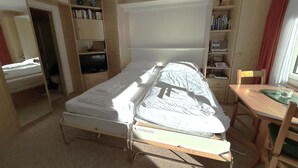Et lille værelse med en enkelt seng, et skrivebord og en bogreol.