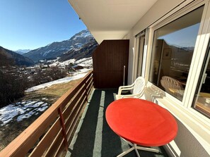 Ein Balkon mit Holzwertkasten, einem roten Tisch und weißen Stühlen.