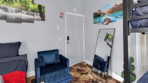 Una habitación con una cama, un sillón azul, un espejo grande y obras de arte en las paredes.