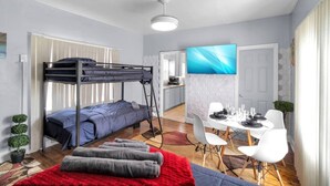 Habitación pequeña con una litera, una mesa de comedor con sillas, un televisor y una kitchenette.