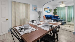 Un comedor con una mesa de madera preparada para cuatro personas, un sofá azul, una lámpara de pie y un cuadro en la pared.