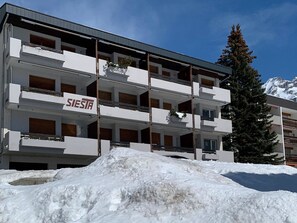 A multi-story hotel with balconies, a sign reading 'SIESTA,' and a snow-covered ground. - Residenz Siesta Leukerbad # 4-bed apartment, Bad, WC by Interhome (Leukerbad)
